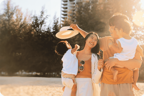 Eine Familie mit zwei kleinen Kindern genießt die Sonne im Sommerurlaub am Strand, um Vitamin D zu tanken.